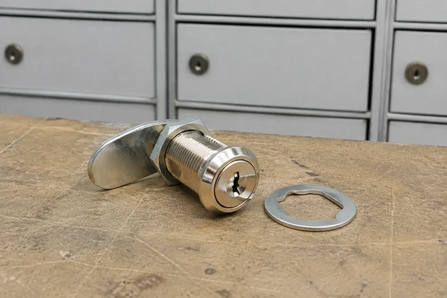 Detached threaded cam lock and mounting washer on a workbench in front of closed mail compartments. — Mailbox Lock Replacement, Kitchener